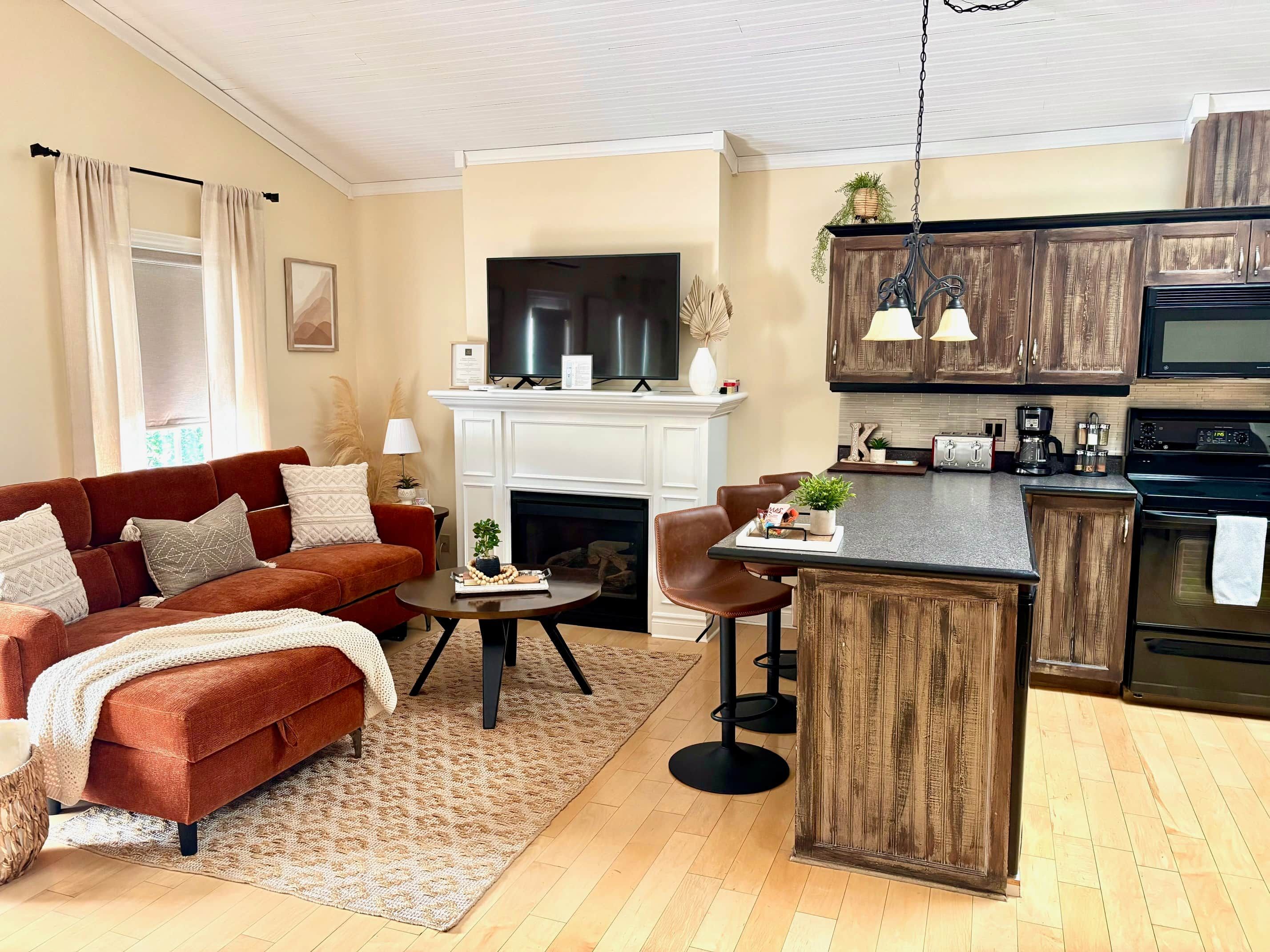 A modern living room with a fireplace, a red sofa, and a kitchen area with wooden cabinets and a black oven.