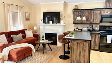 A modern living room with a fireplace, a red sofa, and a kitchen area with wooden cabinets and a black oven.