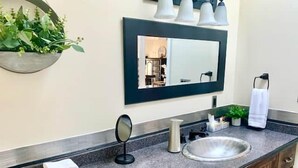 Une salle de bain avec un comptoir en granit, un lavabo rond, un miroir et un porte-serviettes.