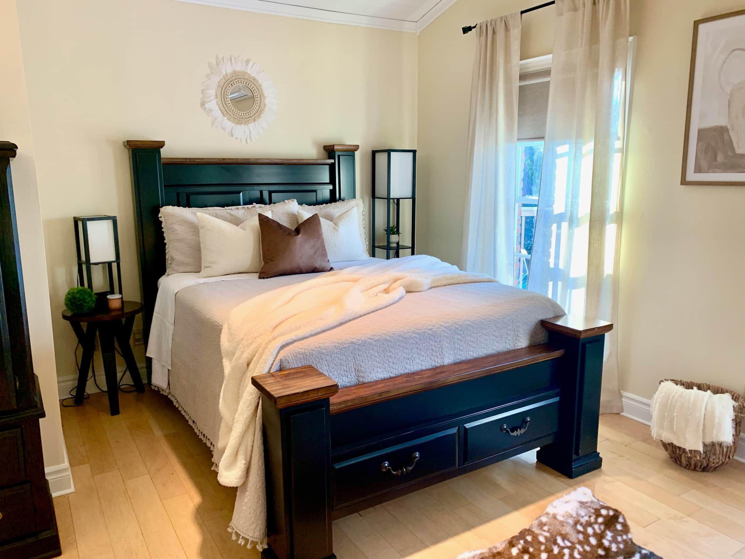 A bedroom with a bed, bedside tables, a nightstand, a window with curtains, and a wall-mounted decoration.