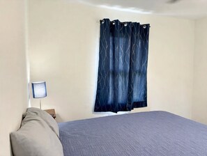 A room with a bed, a nightstand, a lamp, and a window with curtains.