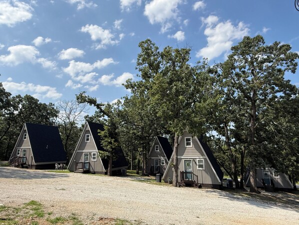 A row of small, triangular-roofed cabins with a gravel driveway and trees in the background.