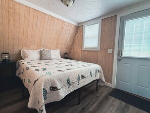 Makuuhuone, jossa on sänky, puuseinät, ikkuna ja ovi.