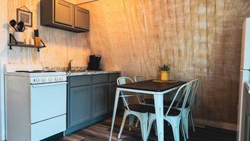 A compact kitchen with a stove, sink, and cabinets, a dining table with chairs, and a wooden wall.