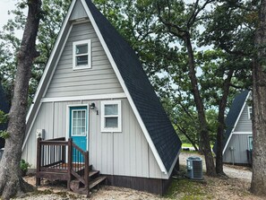 A small, single-story cabin with a front porch and a blue door, surrounded by trees.