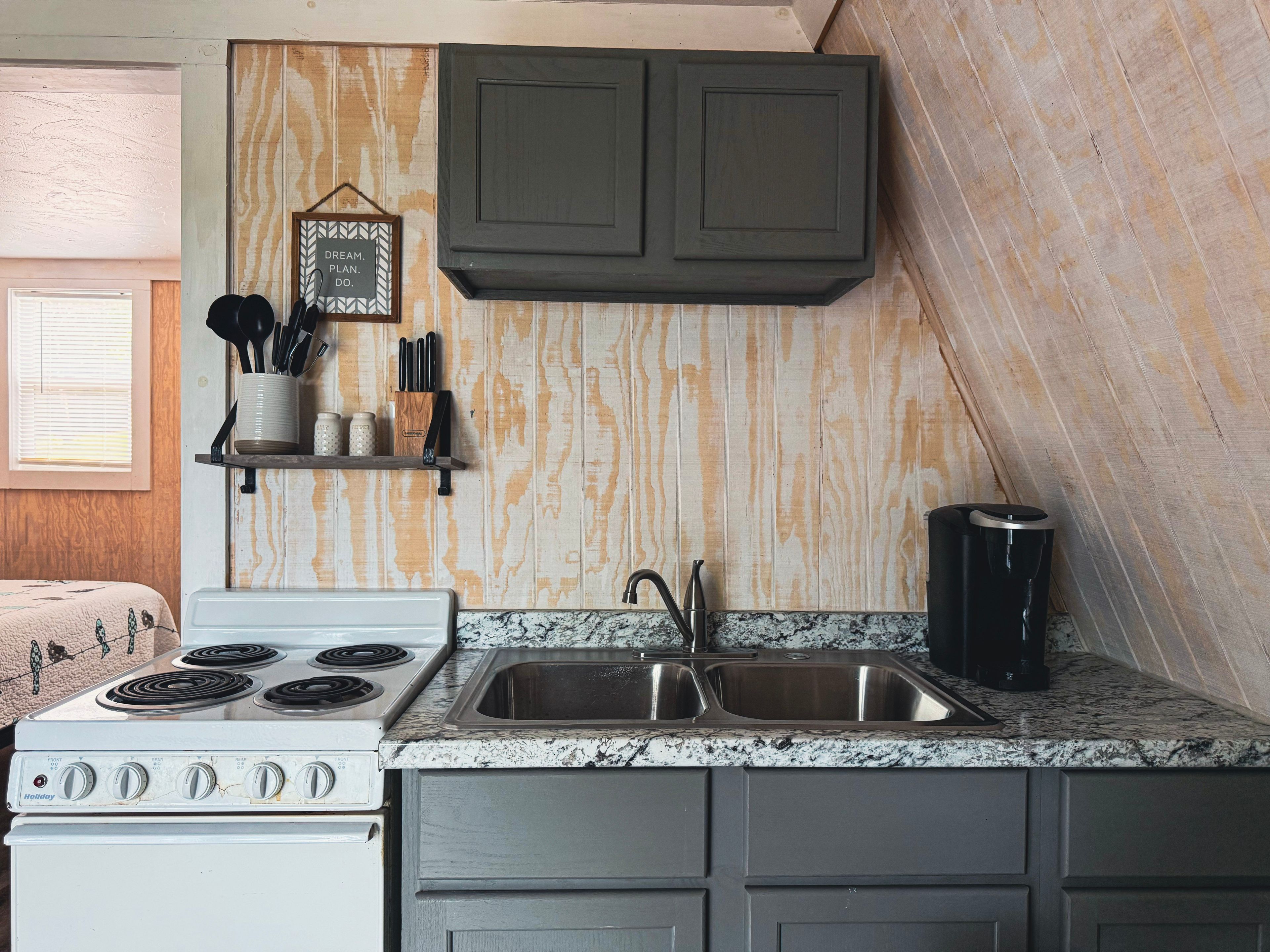 A kitchen with a white stove, a sink, and a wooden backsplash.