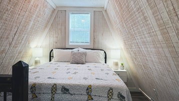 A bedroom with a sloped ceiling, a bed with a patterned quilt, two bedside lamps, and a window with blinds.