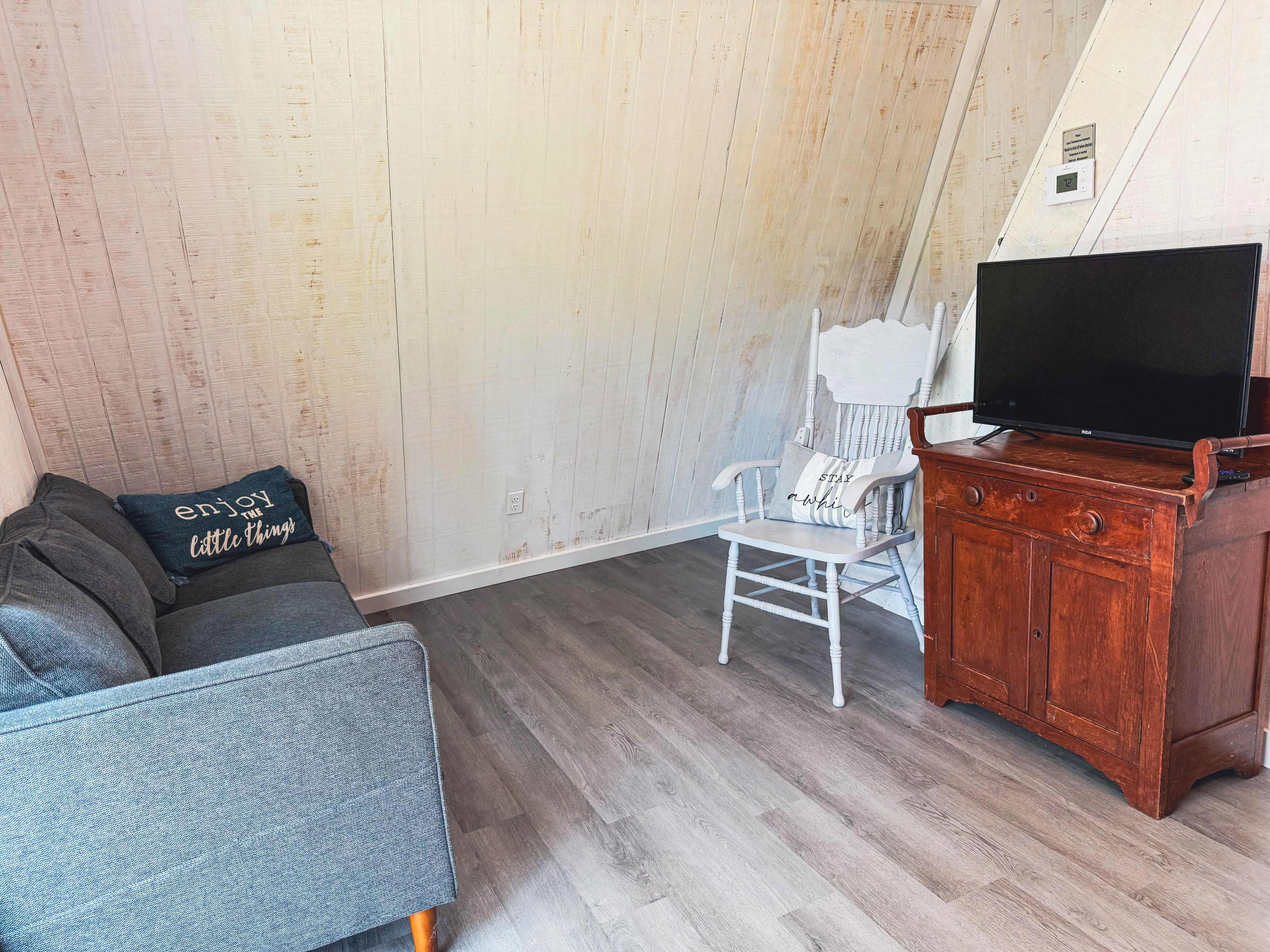 Una habitación con un sofá gris, una silla blanca, un armario de madera y un televisor.