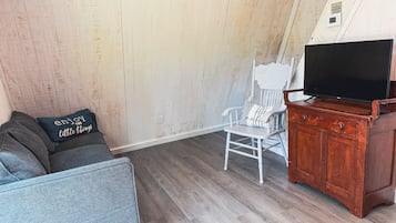 Una habitación con un sofá gris, una silla blanca, un armario de madera y un televisor.