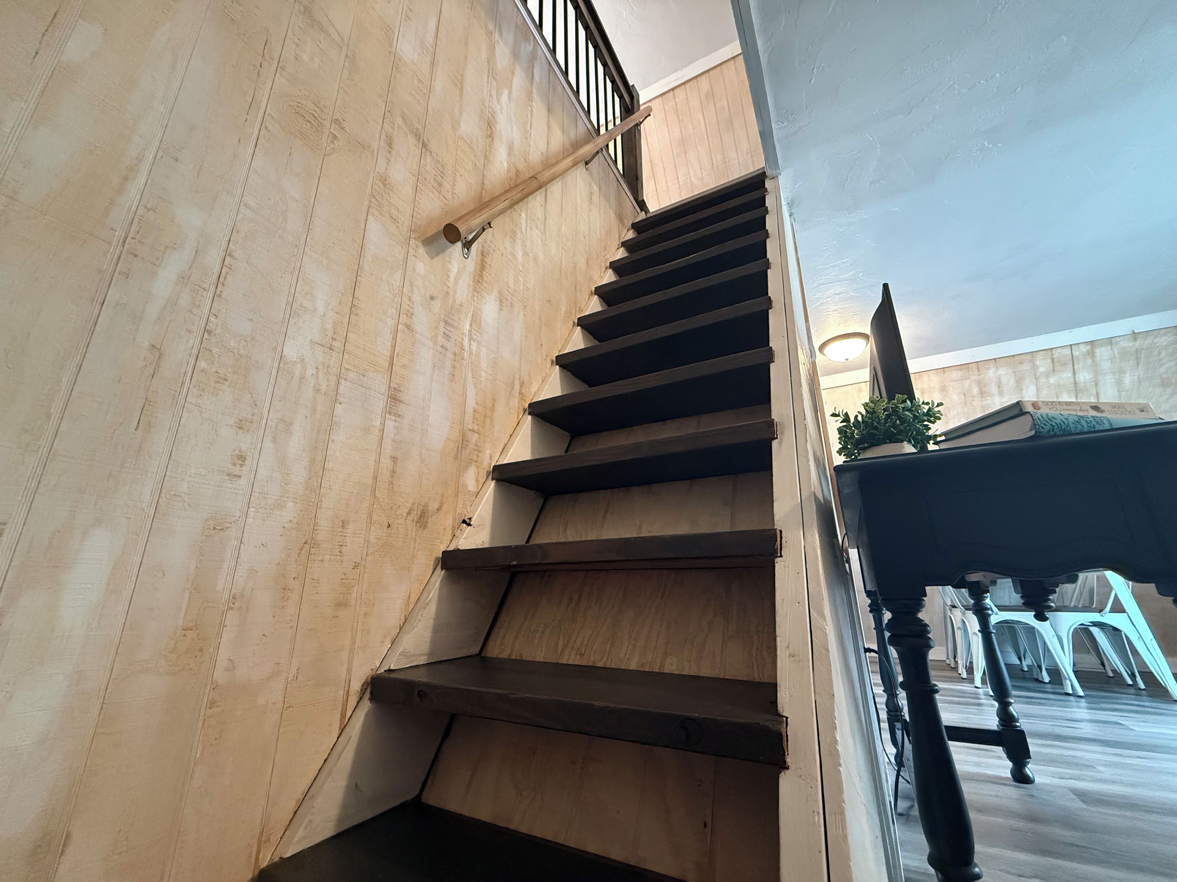 Una escalera de madera con barandilla que lleva a un rellano con una planta en maceta y una mesa con sillas.