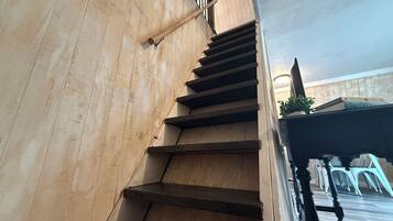 Una escalera de madera con barandilla que lleva a un rellano con una planta en maceta y una mesa con sillas.