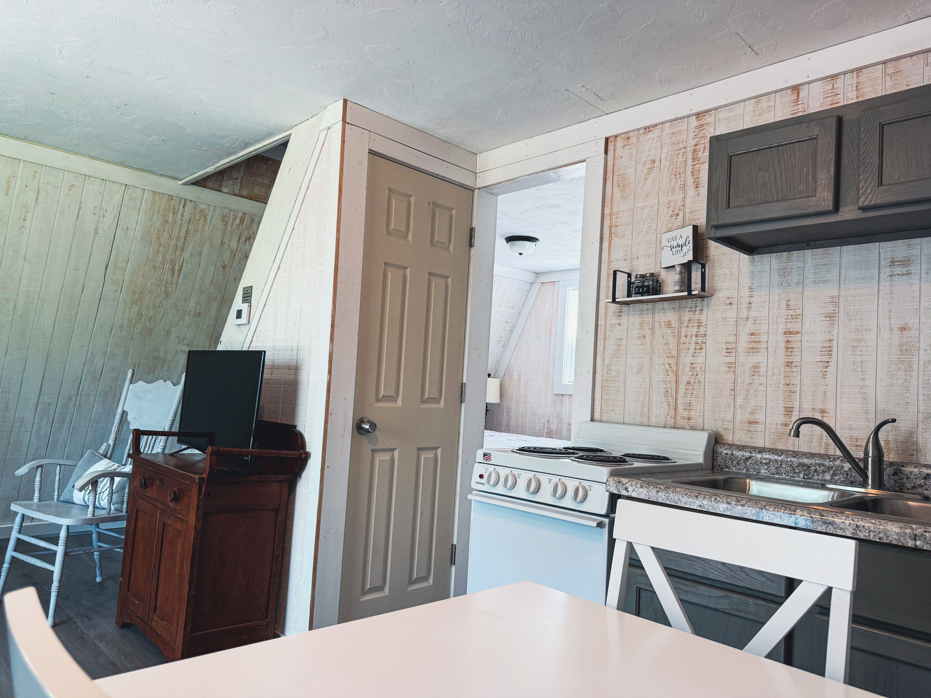 A compact kitchen with a stove, sink, and wooden paneling.