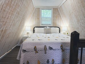 A bedroom with a sloped ceiling, a bed with a patterned duvet, two bedside lamps, and a window with blinds. - Table Rock Lake A-Frame Cabin | Black Oak Lodge 2 (Lampe)