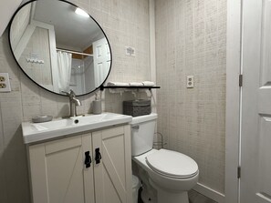 Casa de banho com lavatório branco, espelho redondo, sanita e um porta-toalhas.