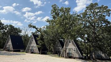 A row of small, triangular-roofed cabins with a gravel driveway and trees in the background.