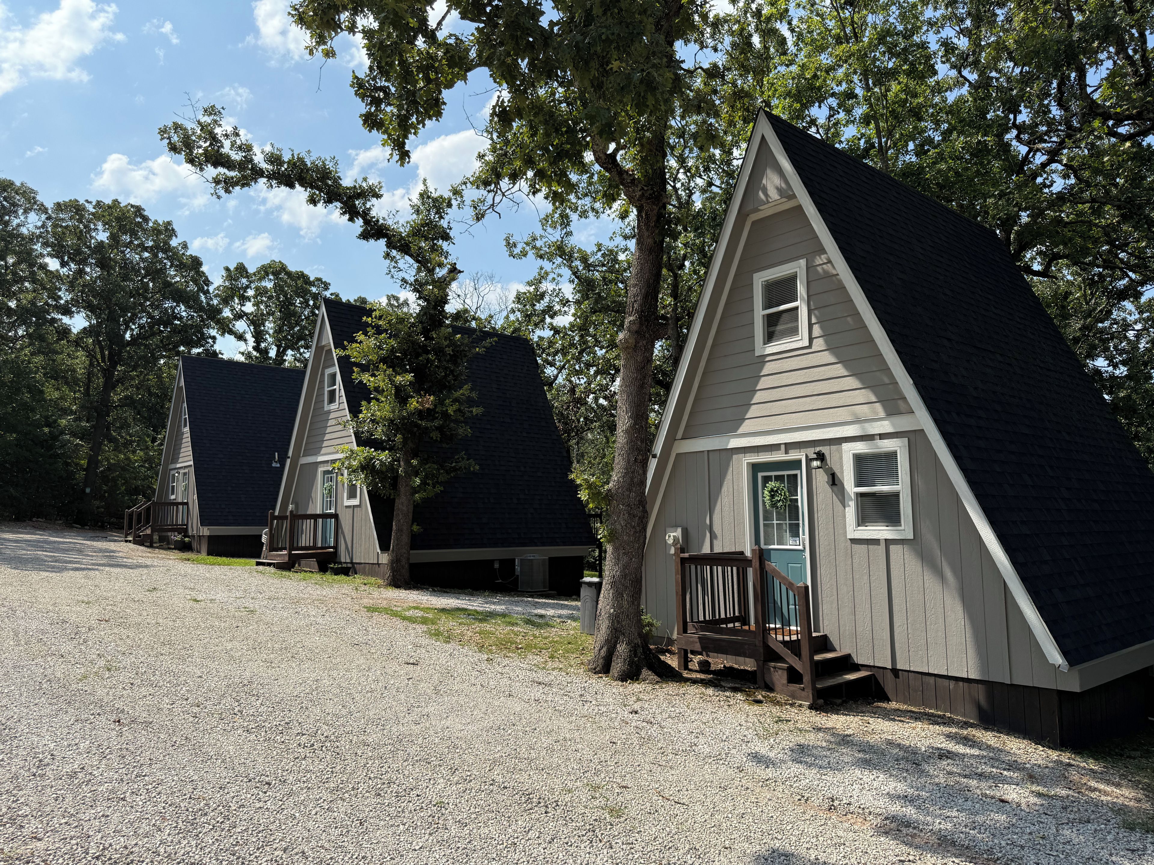 A row of small, triangular cabins with a gravel driveway, surrounded by trees.