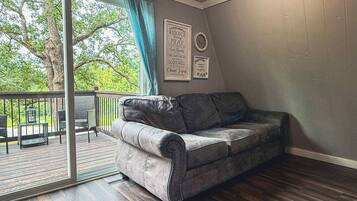 A room with a grey sofa, a sliding glass door leading to a balcony, and a wall with framed inspirational quotes.