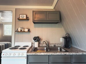 Een keuken met een fornuis, spoelbak en kastjes. Boven het fornuis hangt een bordje met de tekst 'Home Sweet Home'.