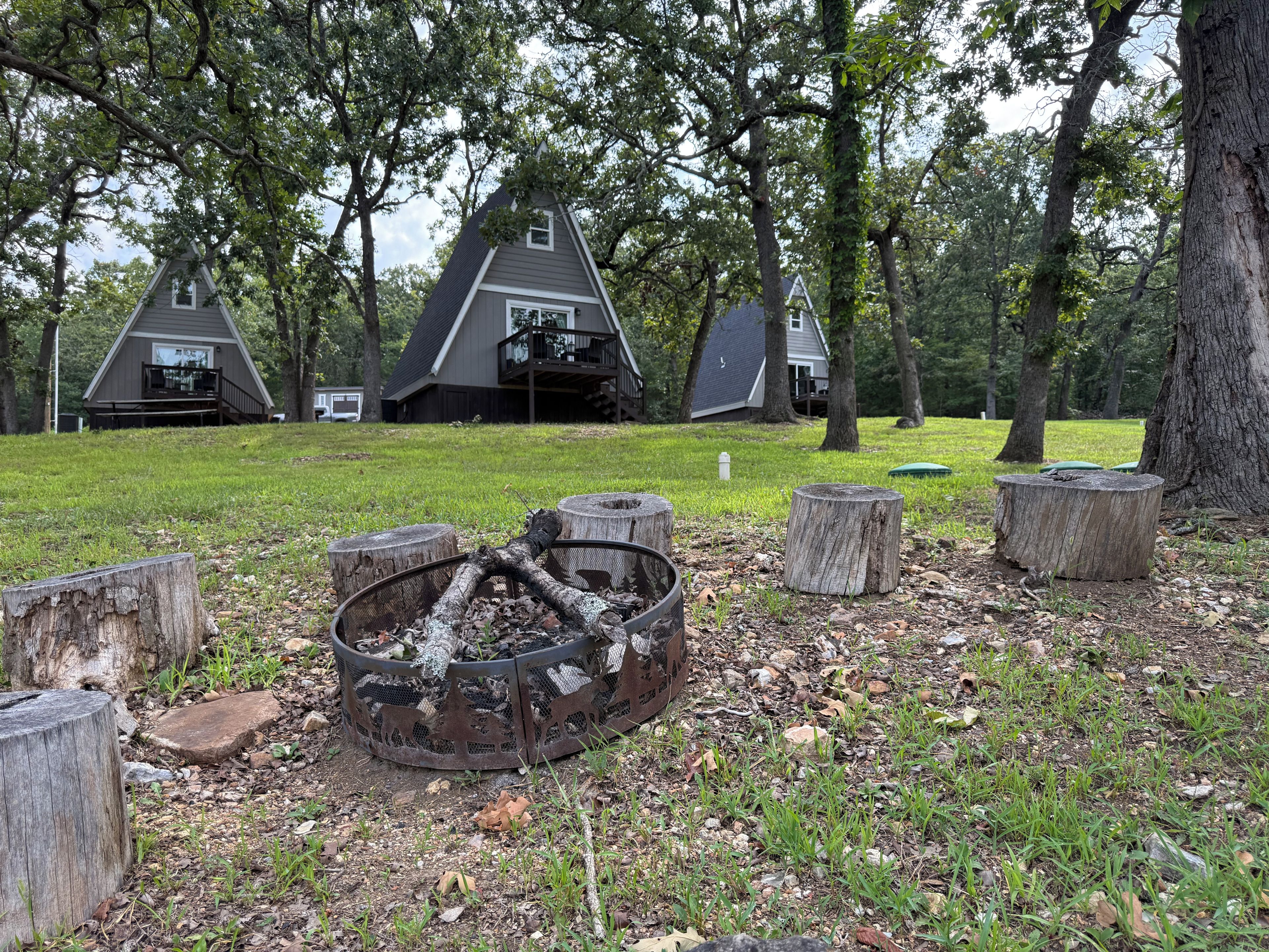 A campsite with three cabins, a fire pit, and surrounding trees.