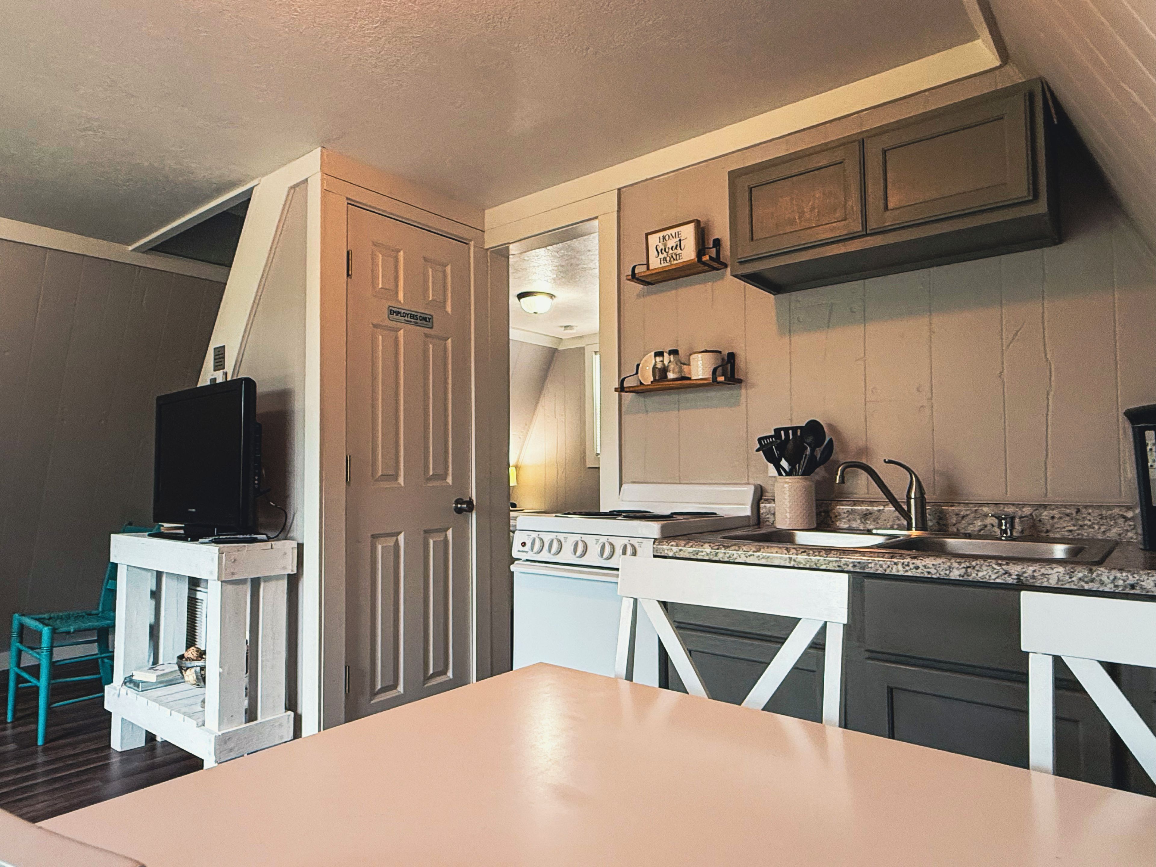 A compact kitchen with a stove, sink, and a television on a small table.
