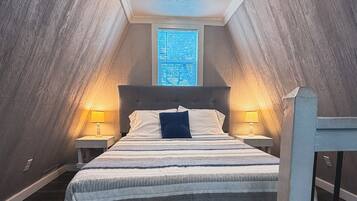 A bedroom with a sloped ceiling, a bed with a headboard, two bedside tables with lamps, and a window with blinds.