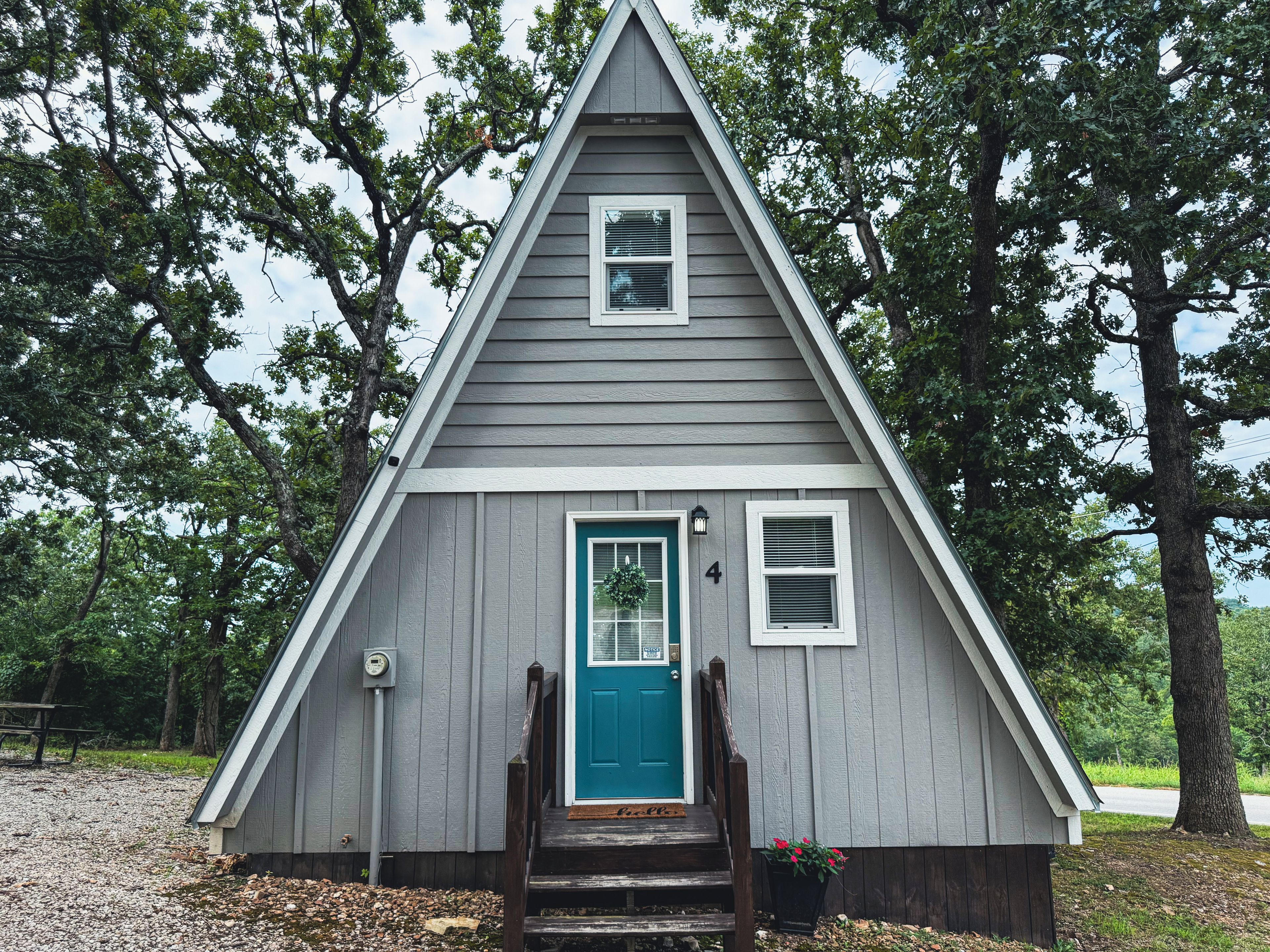 A small, single-story cabin with a steeply pitched roof, a front door with a green door frame, and a small porch with steps leading up to it.