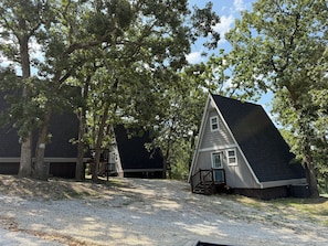 Een huis met een steile dakschildering, omgeven door bomen en grind.