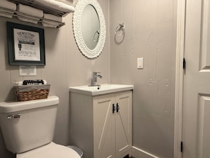 Un baño con inodoro, lavamanos, espejo y un cartel enmarcado.