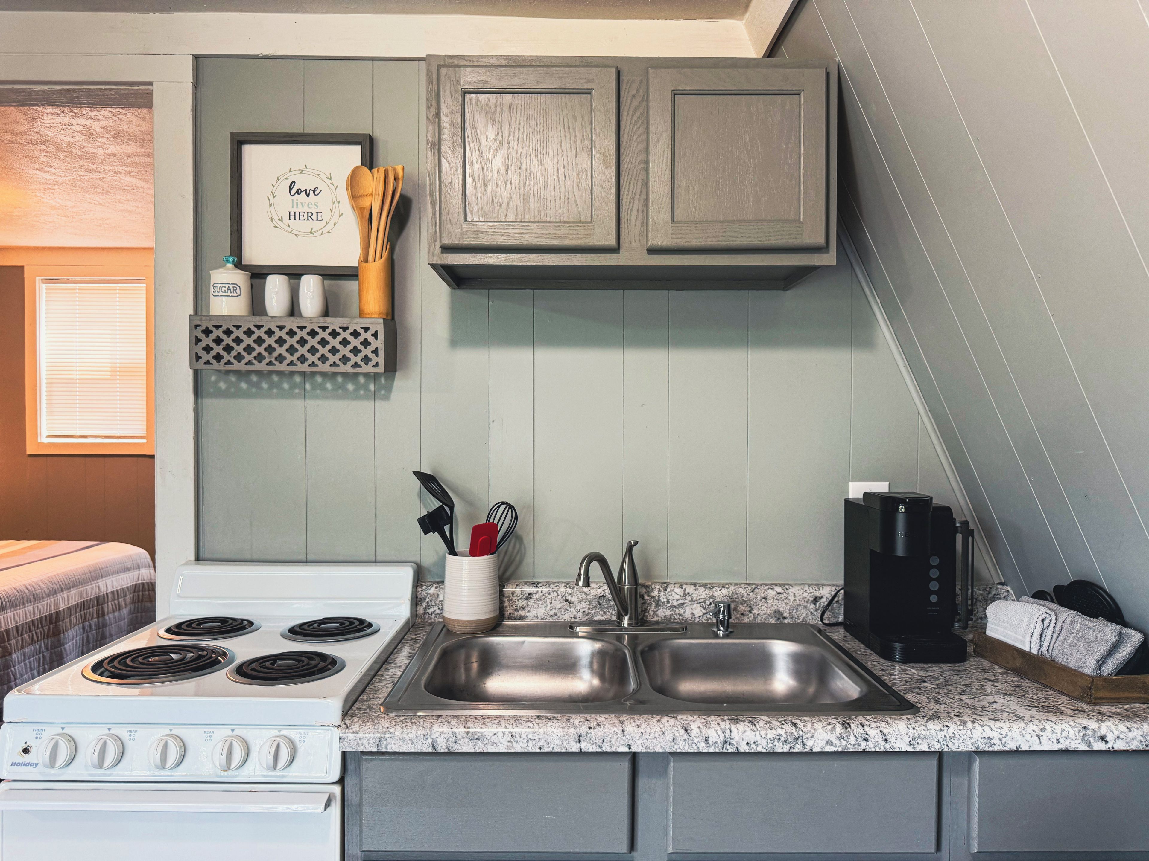 A kitchen with a white stove, two sinks, wooden cabinets, and a framed sign on the wall.