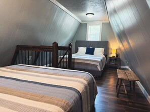 Quarto com duas camas, um banco de madeira, uma mesa de cabeceira e uma janela.