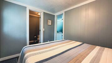 A bedroom with a bed, a door leading to a bathroom, and a wall-mounted light fixture.