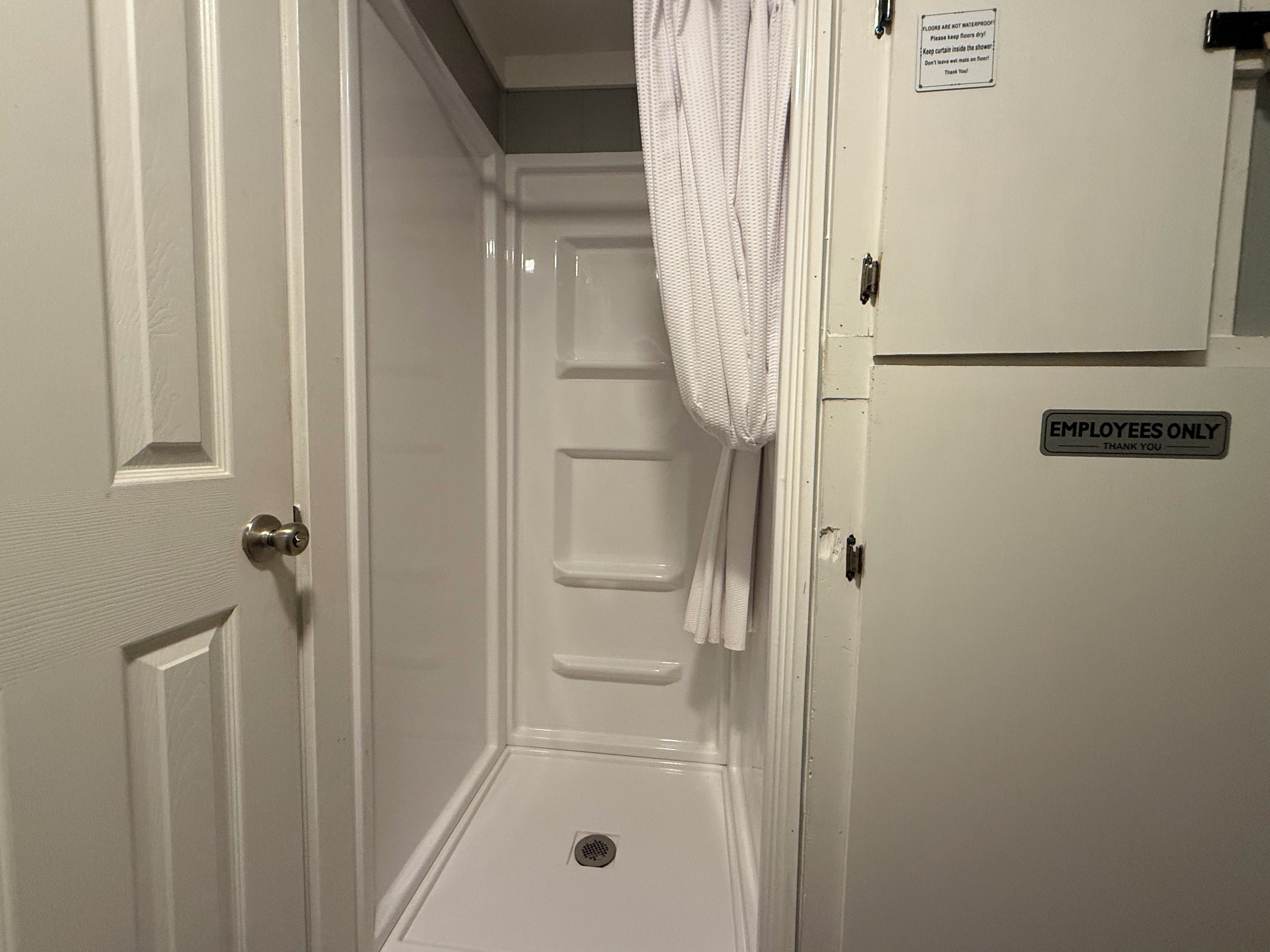 A bathroom with a shower, a towel hanging on the wall, and an 'EMPLOYEES ONLY' sign.