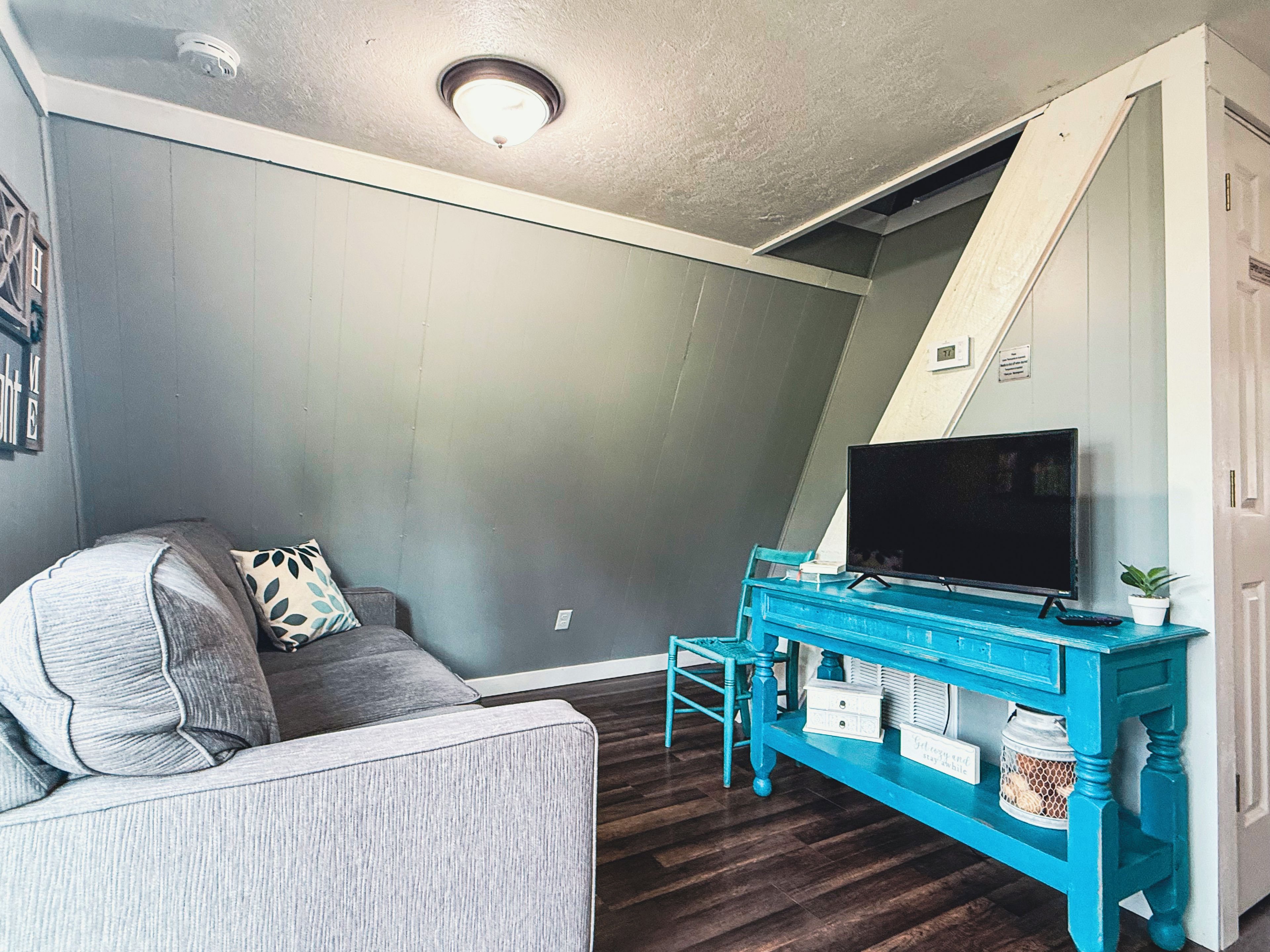 A living room with a grey couch, a teal entertainment unit, and a flat-screen TV.