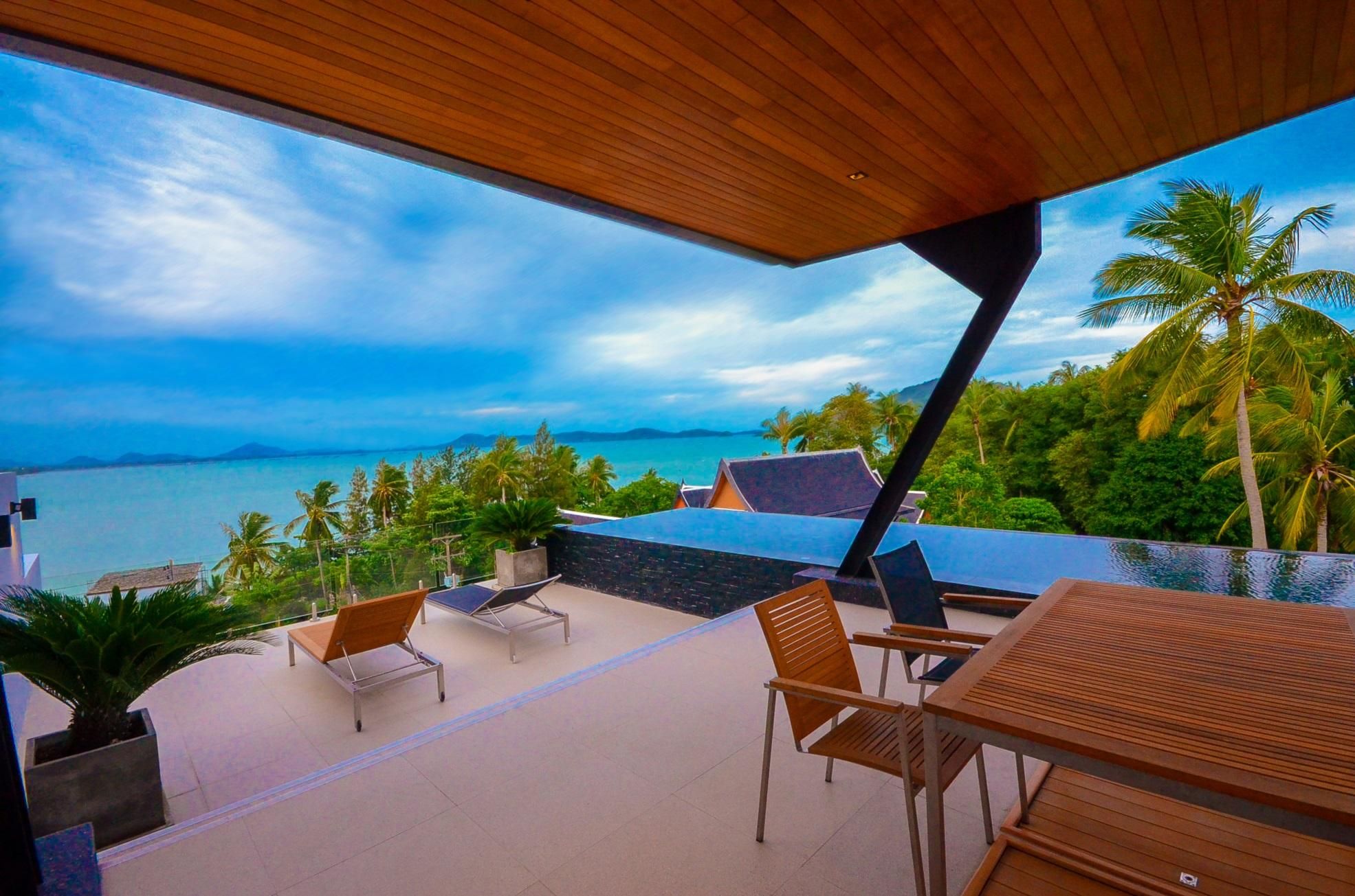 Una terraza moderna al aire libre con vista al mar, amueblada con mobiliario de madera y una piscina.