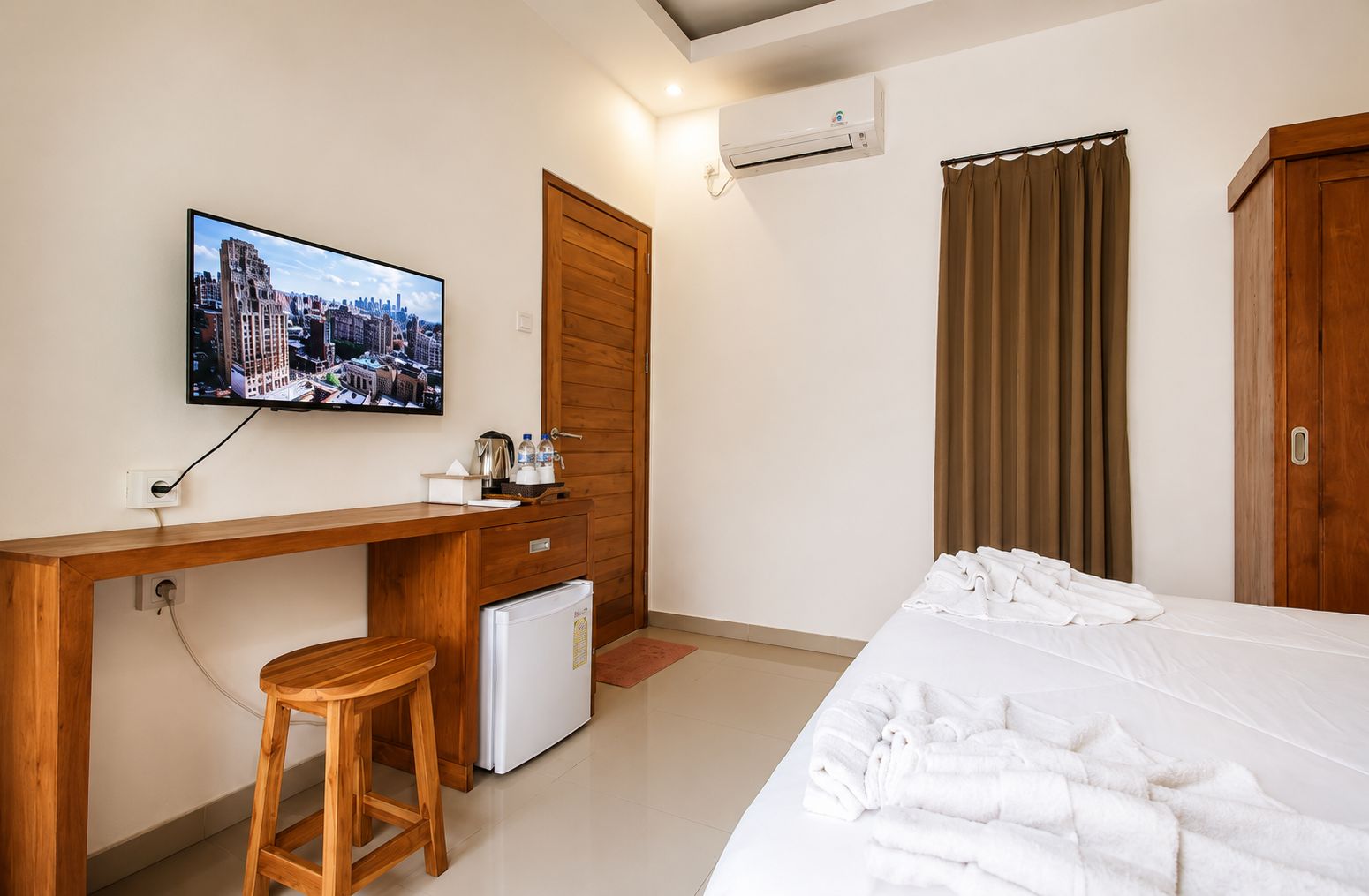 A hotel room with a bed, a desk with a chair, a television, a refrigerator, and a window with curtains.