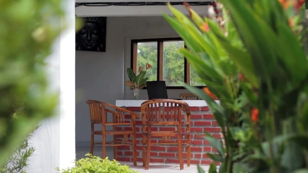 Un coin repas avec un mur en briques, deux chaises en bois, une table noire et une fenêtre donnant sur un paysage verdoyant.