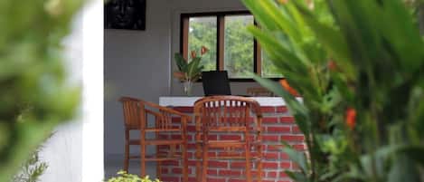 Comedor con pared de ladrillo, dos sillas de madera, una mesa negra y una ventana con vista a la vegetación.
