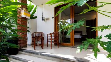 A room with a bed, a wooden chair, a potted plant, and a brick wall.