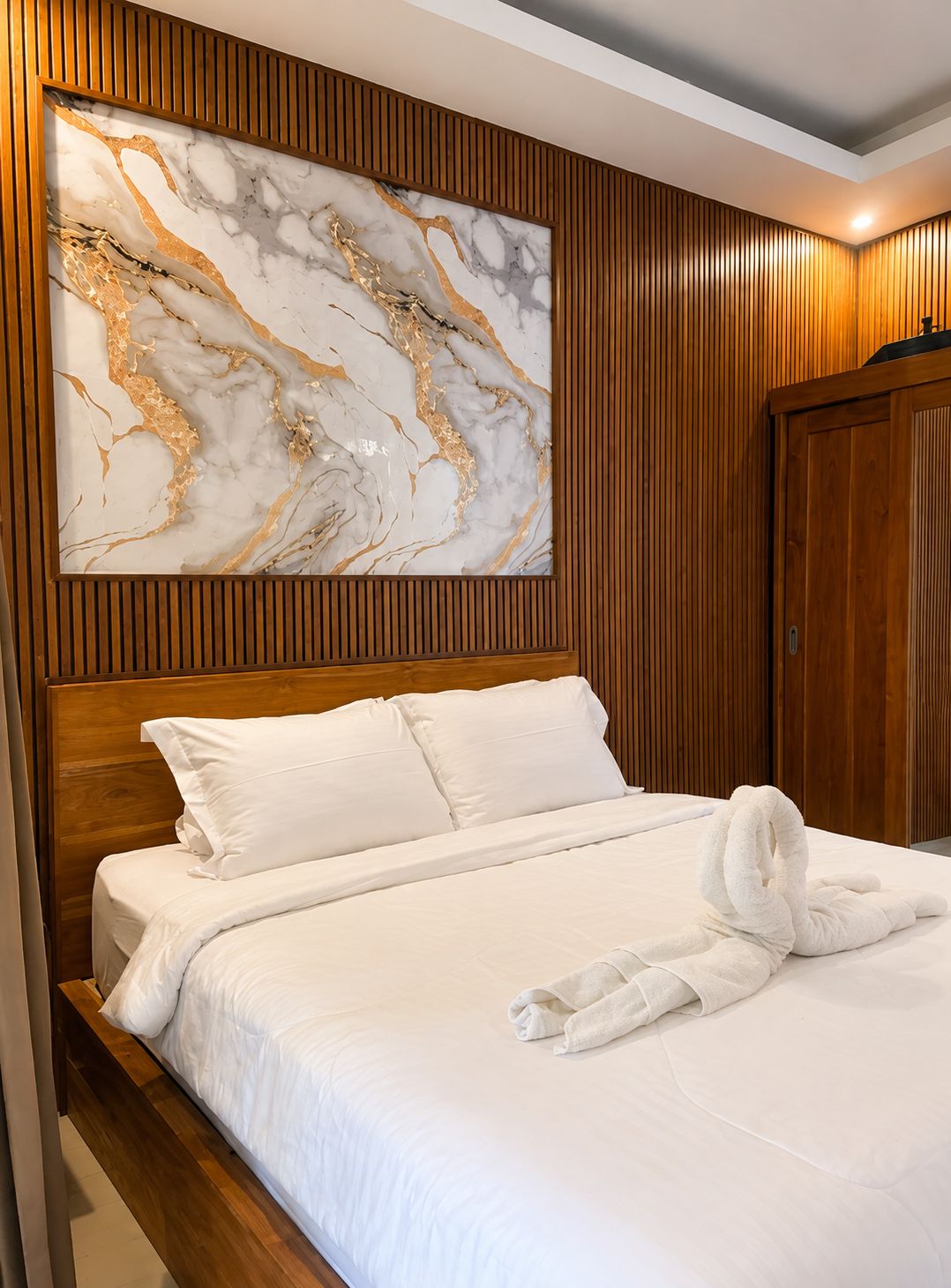 A hotel room with a wooden headboard, a marble artwork, and a neatly made bed.