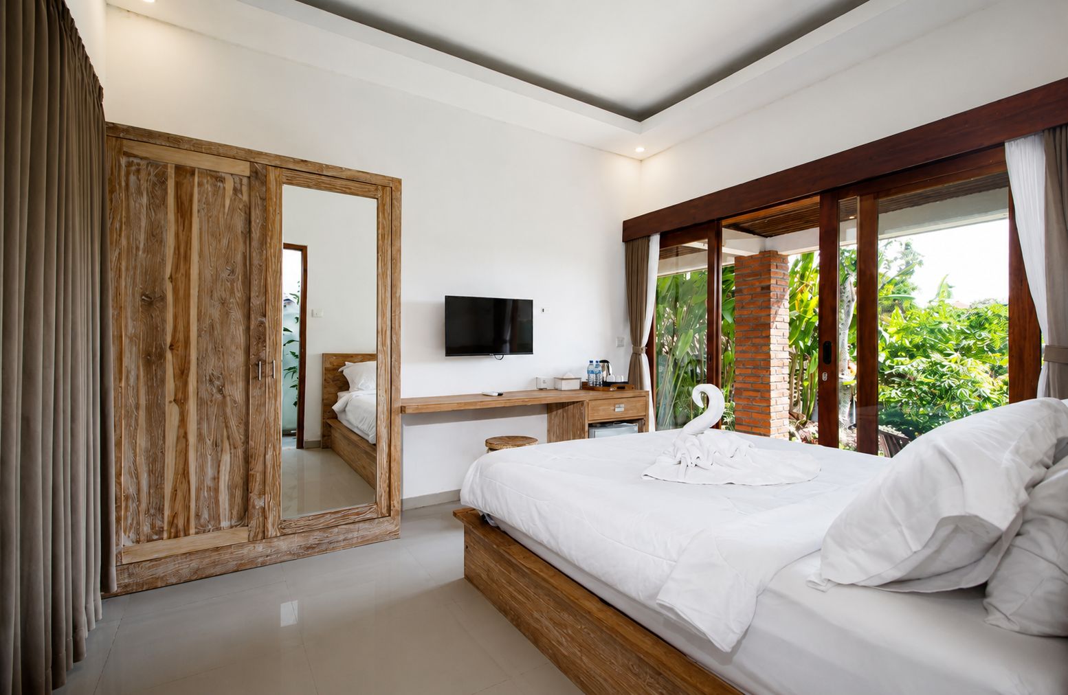 A bedroom with a bed, a desk, a television, and a large mirror.