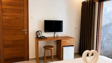 A hotel room with a wooden desk, a television, a small refrigerator, a bed with a swan-shaped pillow, and a window with curtains.