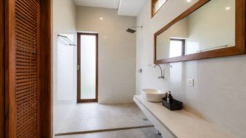A modern bathroom with a large mirror, a round sink, and a shower.