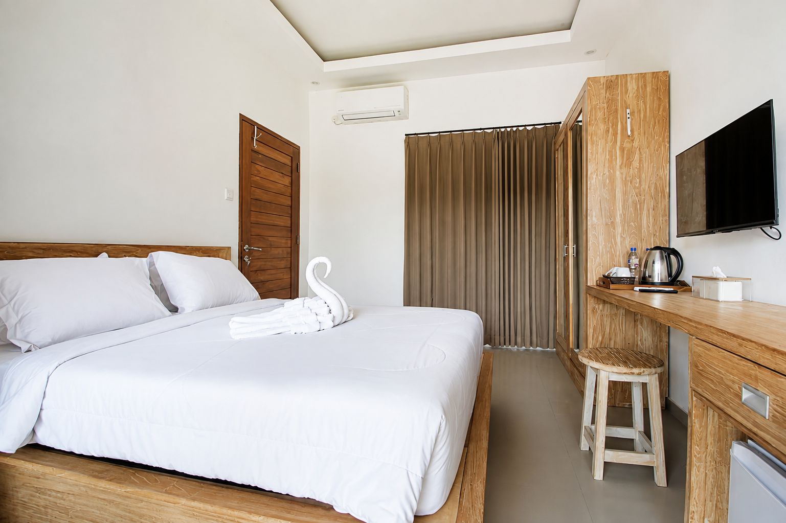 A hotel room with a bed, a wooden desk, a television, and a shower area.