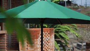 Une terrasse en briques avec une table ronde et quatre tabourets, un parasol et un mur en briques.