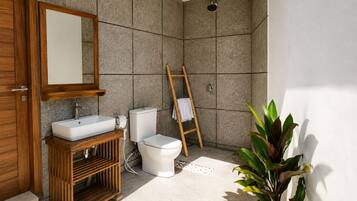A bathroom with a wooden vanity, a white sink, a toilet, and a shower area with a bamboo ladder.