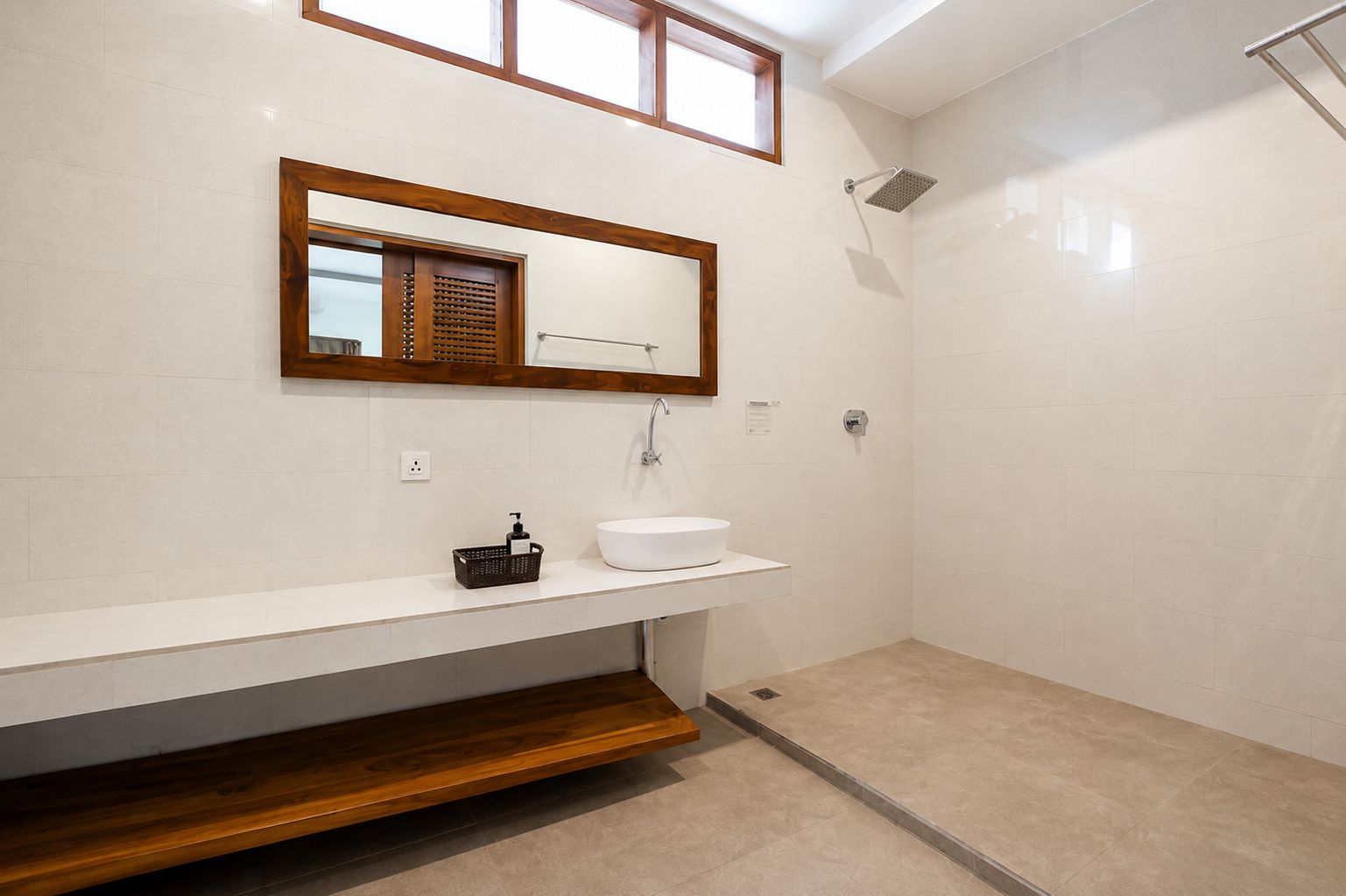 A bathroom with a white sink, wooden vanity, and a shower area.
