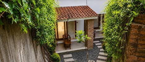 Un patio con techo de tejas, una silla de madera y una planta pequeña.