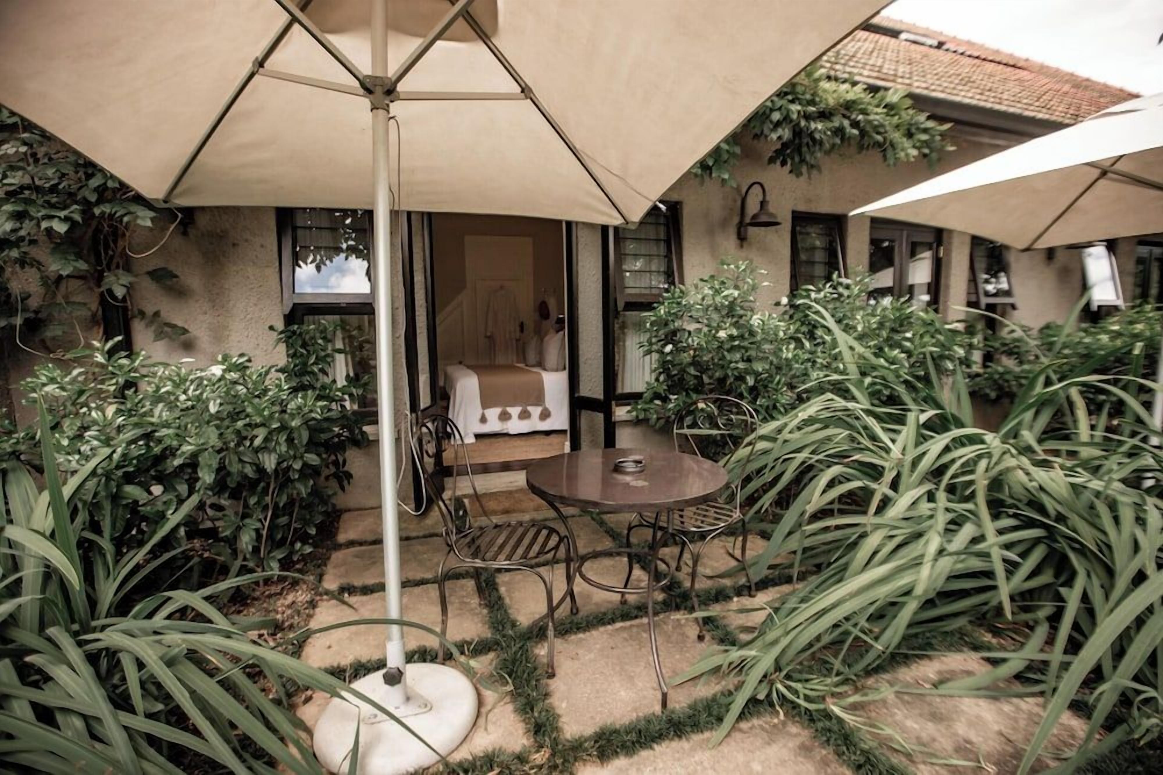 An outdoor patio area with a round table and chairs, surrounded by plants and umbrellas.