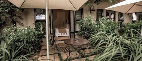 An outdoor patio area with a round table and chairs, surrounded by plants and umbrellas.
