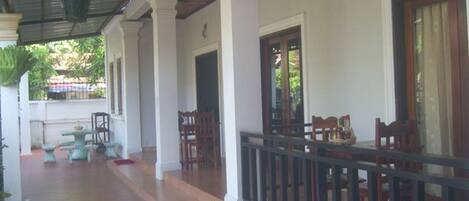 A covered porch with a railing, wooden chairs, and a table.